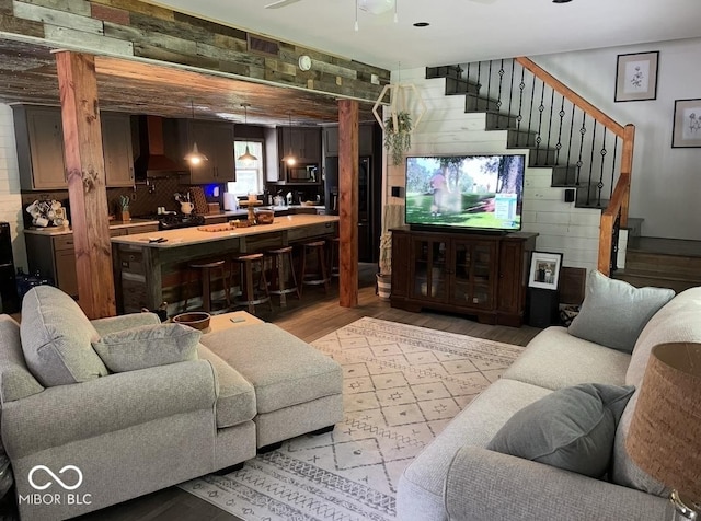 living area featuring wood walls, light wood-style flooring, stairs, and a ceiling fan