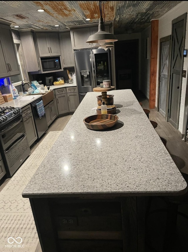 kitchen with light wood-style flooring, a center island, light stone countertops, black appliances, and pendant lighting