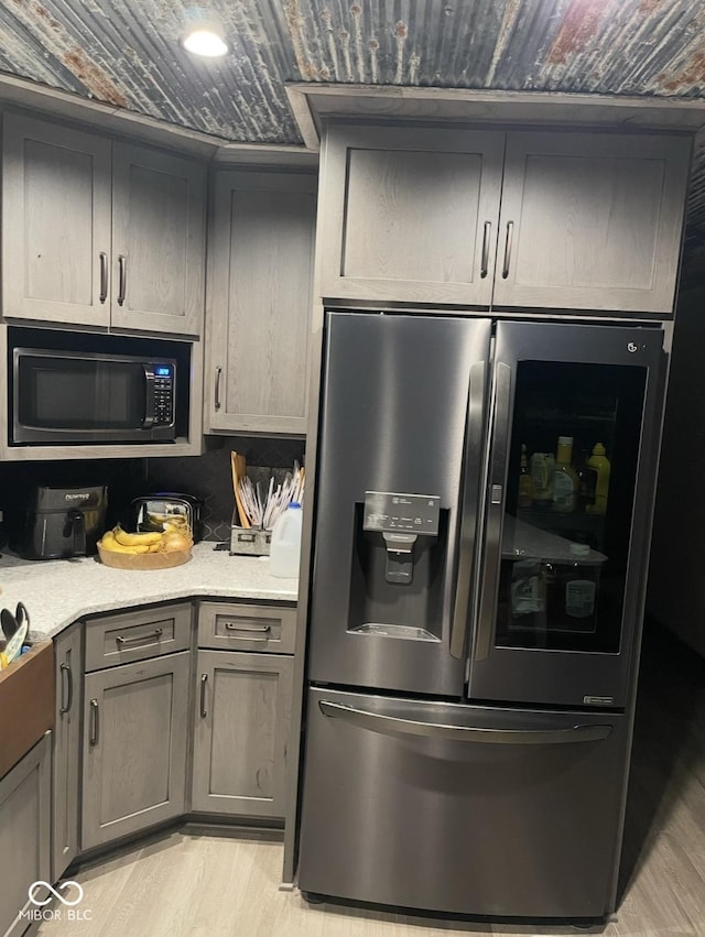 kitchen featuring gray cabinetry, light wood-style floors, light stone countertops, black microwave, and stainless steel fridge with ice dispenser