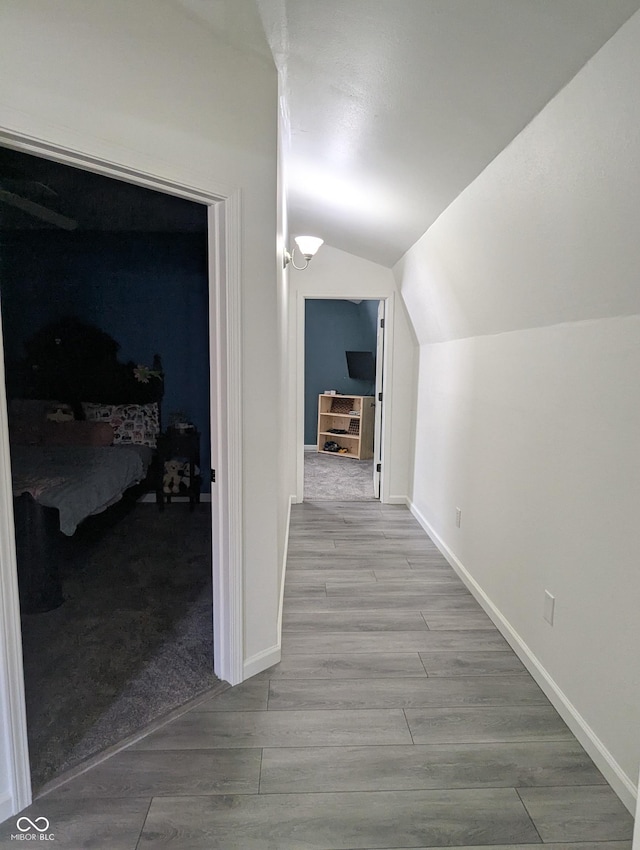 hallway featuring lofted ceiling, baseboards, and wood finished floors