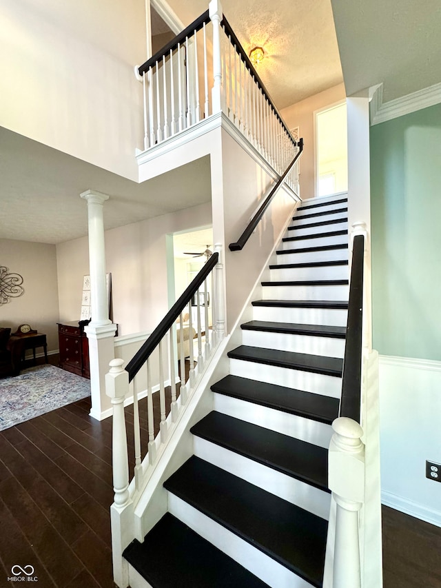 stairs featuring ornate columns, a high ceiling, baseboards, and wood finished floors