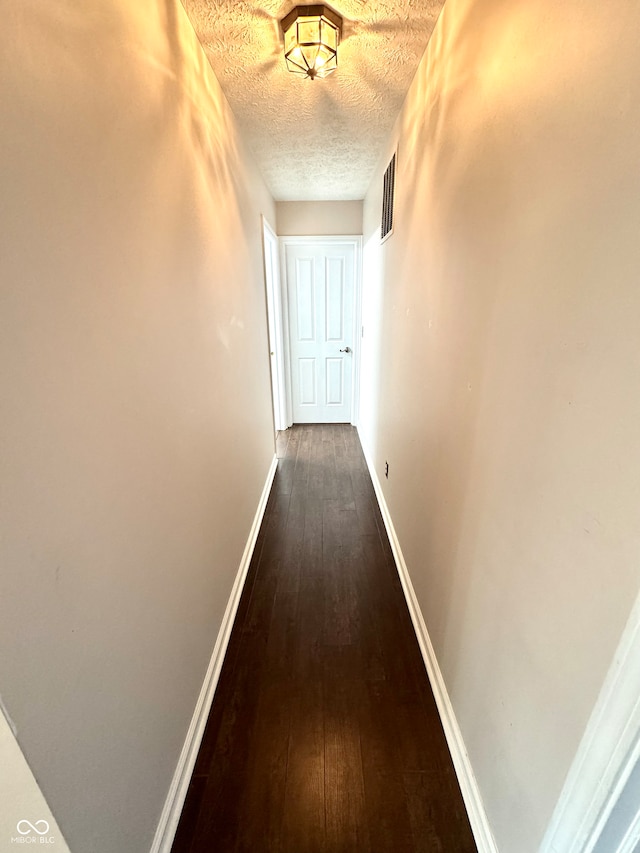 corridor featuring dark wood-style floors, visible vents, a textured ceiling, and baseboards