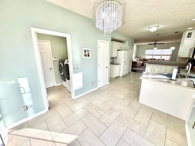 kitchen with washing machine and clothes dryer, open floor plan, white cabinets, a sink, and a textured ceiling