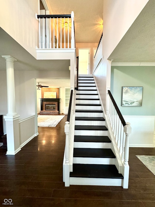 stairs featuring decorative columns, a brick fireplace, ceiling fan, a textured ceiling, and wood finished floors