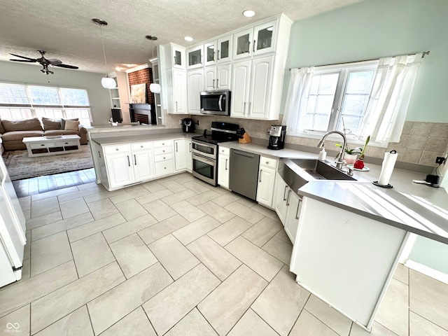 kitchen with glass insert cabinets, open floor plan, a peninsula, stainless steel appliances, and a sink