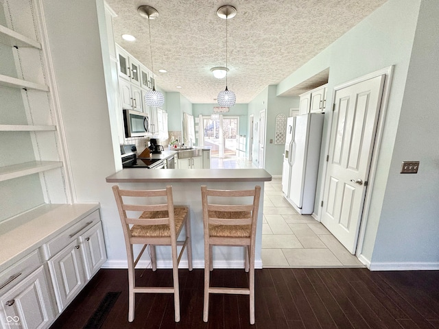 kitchen with stainless steel appliances, white cabinets, a textured ceiling, wood finished floors, and a peninsula