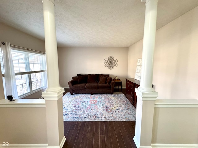 living room featuring a textured ceiling, dark wood-type flooring, baseboards, and ornate columns