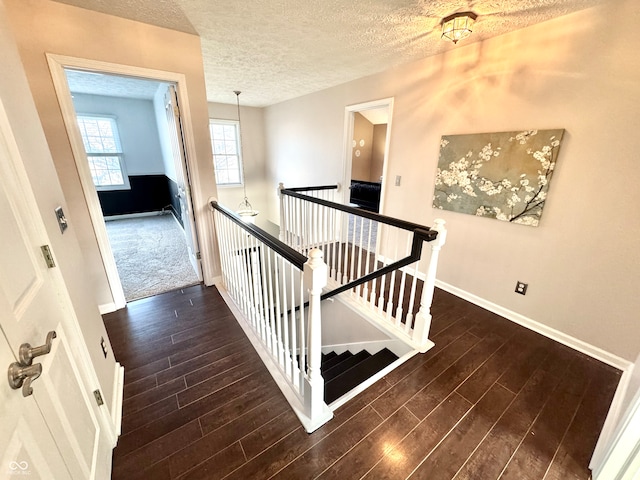 stairway with a textured ceiling, baseboards, and wood finished floors