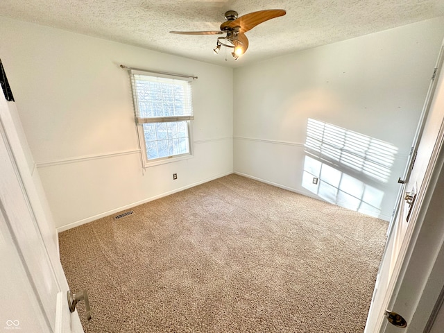 unfurnished room with carpet, visible vents, ceiling fan, and a textured ceiling