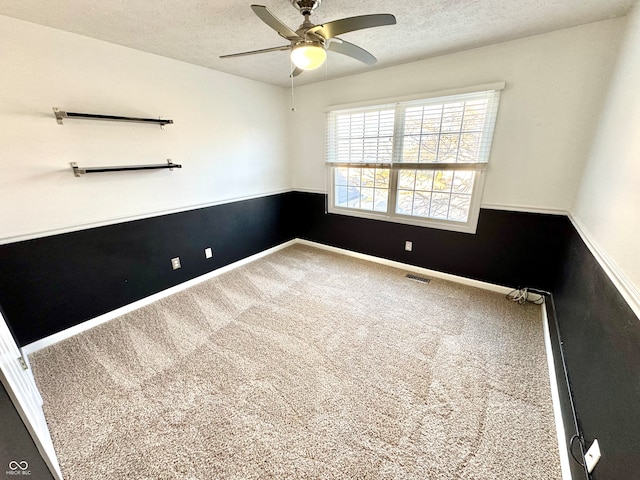 spare room with carpet floors, visible vents, a textured ceiling, and a ceiling fan