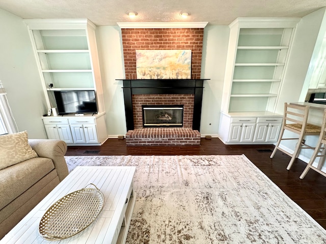 living room featuring a brick fireplace, built in shelves, dark wood-style flooring, and a textured ceiling