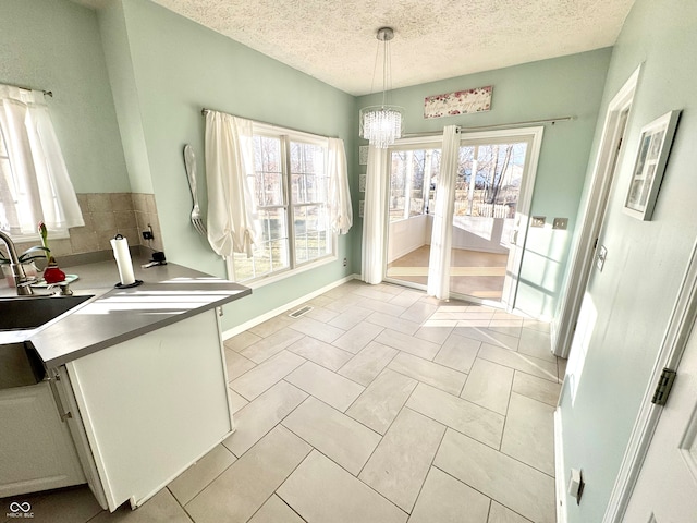 unfurnished dining area featuring a textured ceiling, plenty of natural light, a sink, and visible vents