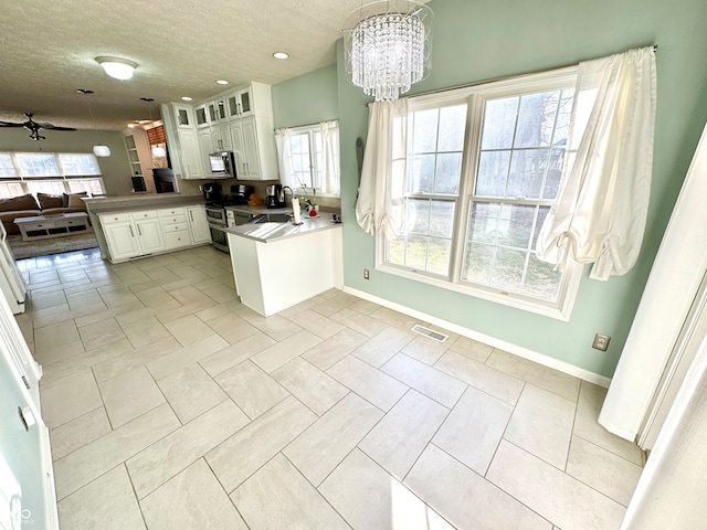 kitchen featuring decorative light fixtures, a peninsula, open floor plan, appliances with stainless steel finishes, and glass insert cabinets