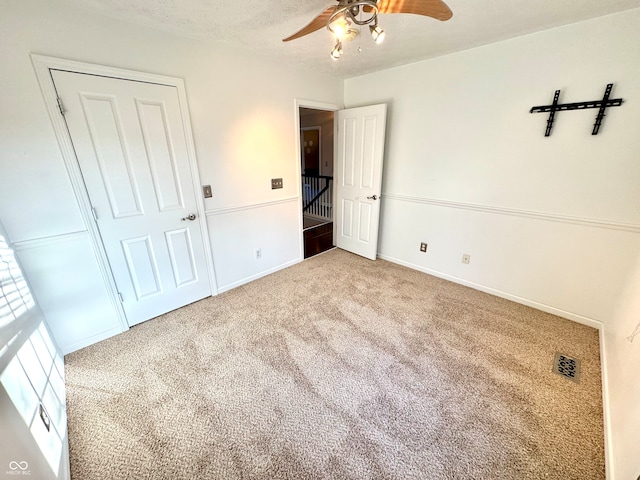 unfurnished bedroom featuring a textured ceiling, carpet flooring, a ceiling fan, visible vents, and baseboards