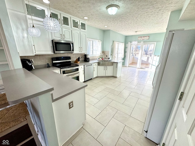 kitchen with white cabinets, a peninsula, hanging light fixtures, stainless steel appliances, and backsplash