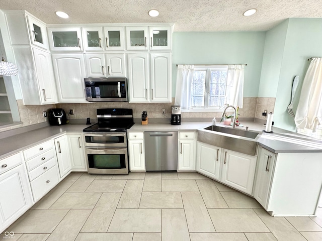 kitchen with stainless steel appliances, white cabinets, a sink, and glass insert cabinets