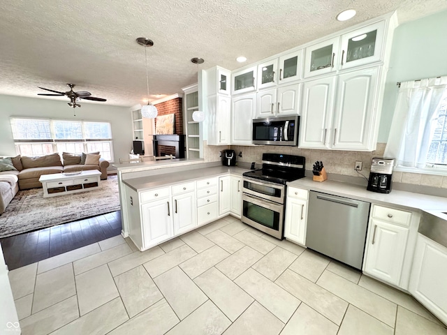 kitchen featuring white cabinets, appliances with stainless steel finishes, open floor plan, glass insert cabinets, and light countertops