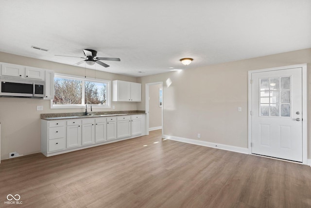 kitchen featuring visible vents, light wood-style floors, white cabinets, ceiling fan, and baseboards