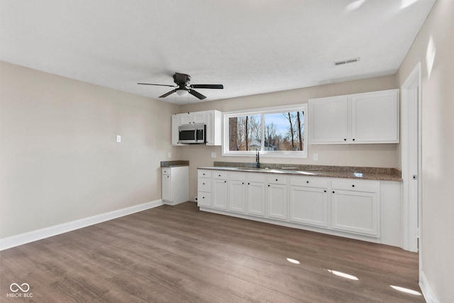 kitchen featuring baseboards, stainless steel microwave, white cabinets, and wood finished floors