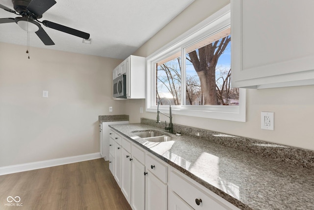 kitchen with dark wood-type flooring, white cabinets, stainless steel microwave, and a sink