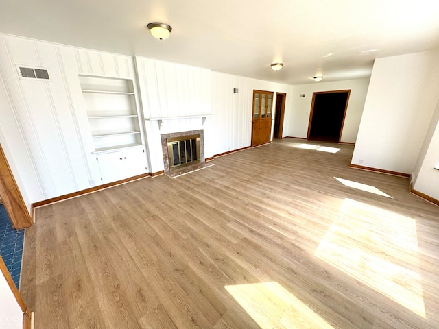 unfurnished living room featuring baseboards, a glass covered fireplace, visible vents, and light wood-style floors