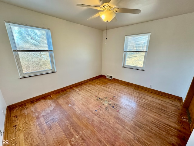 unfurnished room with a healthy amount of sunlight, visible vents, baseboards, and wood finished floors