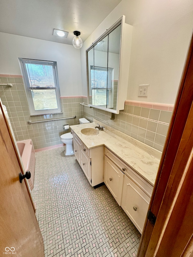 bathroom with a healthy amount of sunlight, tile walls, toilet, and vanity