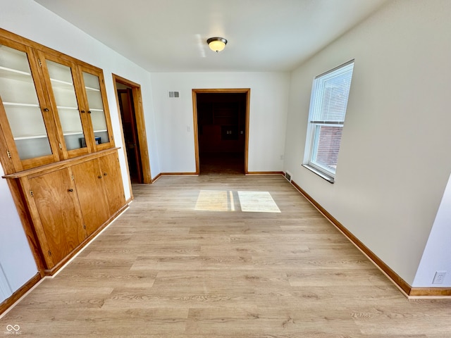 hallway with baseboards, visible vents, and light wood finished floors