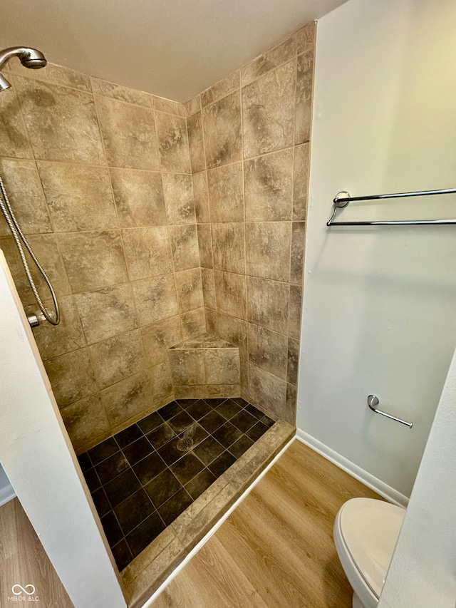 bathroom with toilet, tiled shower, and wood finished floors