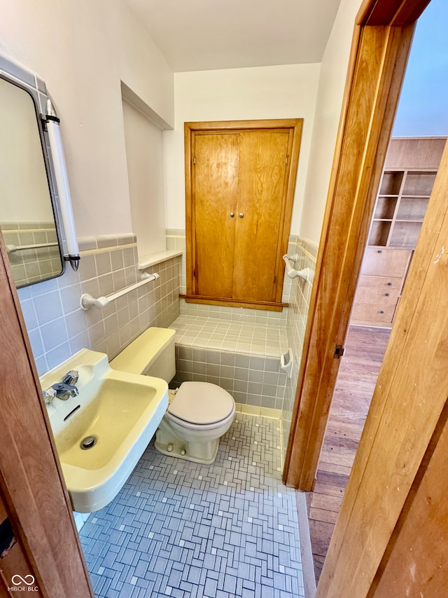 bathroom with toilet, a wainscoted wall, a sink, tile walls, and tile patterned floors