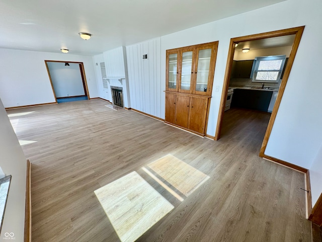 unfurnished living room featuring light wood-style floors, a fireplace with flush hearth, and baseboards