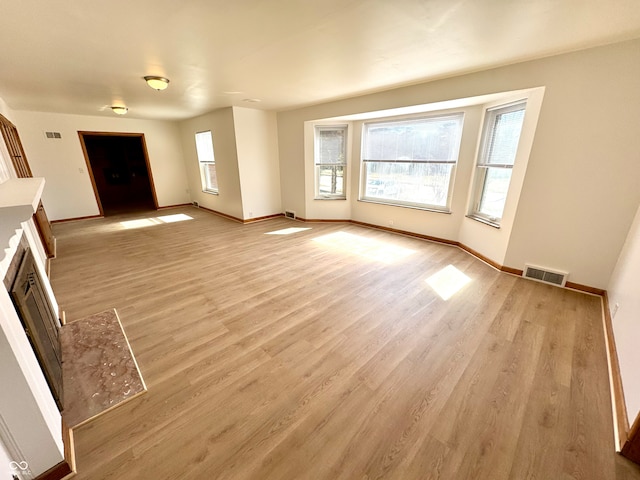 unfurnished living room featuring light wood-type flooring, a fireplace with flush hearth, visible vents, and baseboards