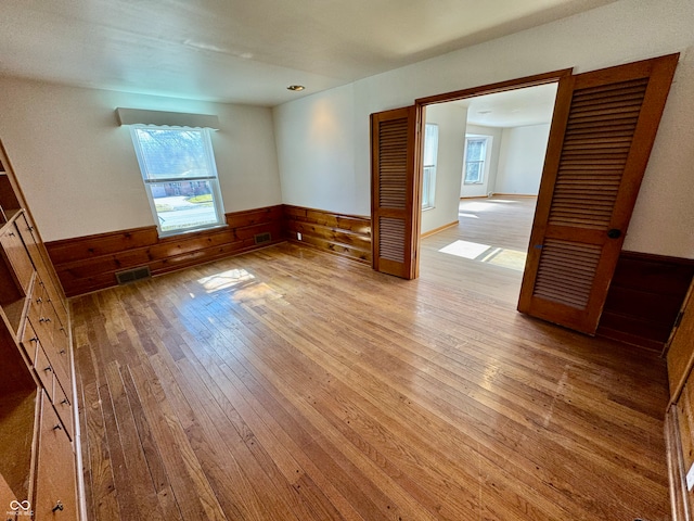 unfurnished room featuring wainscoting, light wood-type flooring, and visible vents