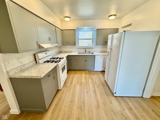 kitchen featuring white appliances, under cabinet range hood, a sink, and gray cabinetry