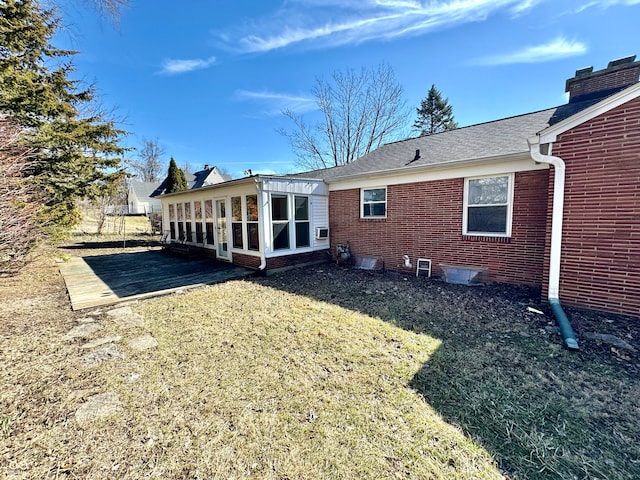 rear view of property featuring brick siding, a chimney, a shingled roof, a lawn, and a sunroom