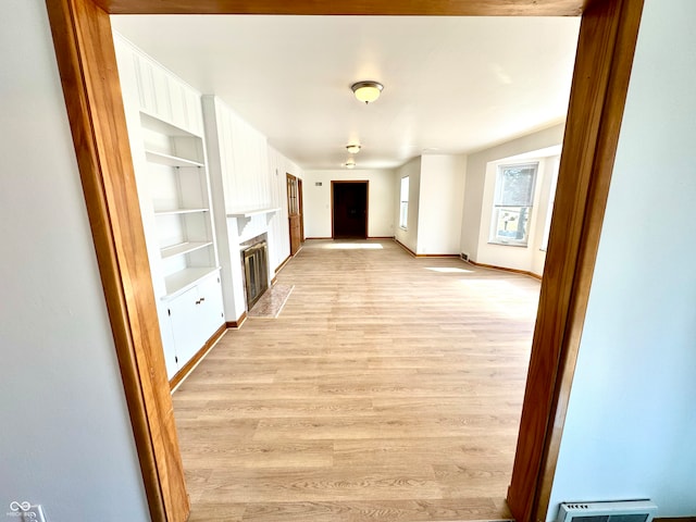 unfurnished living room featuring baseboards, a fireplace with flush hearth, light wood-style flooring, and built in features