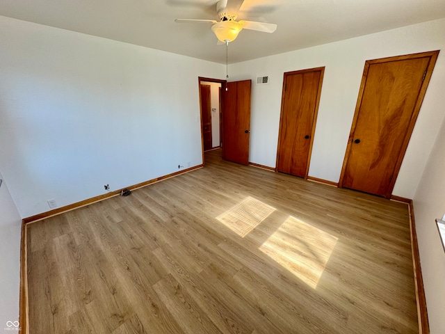 unfurnished bedroom with multiple closets, baseboards, visible vents, and light wood finished floors