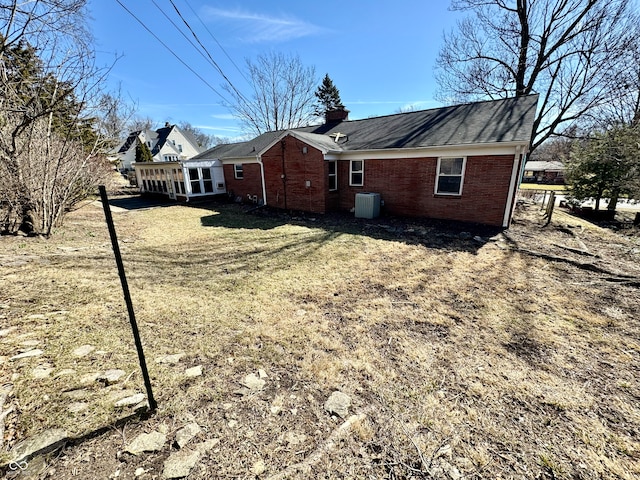 view of side of property featuring a chimney, central AC unit, and brick siding