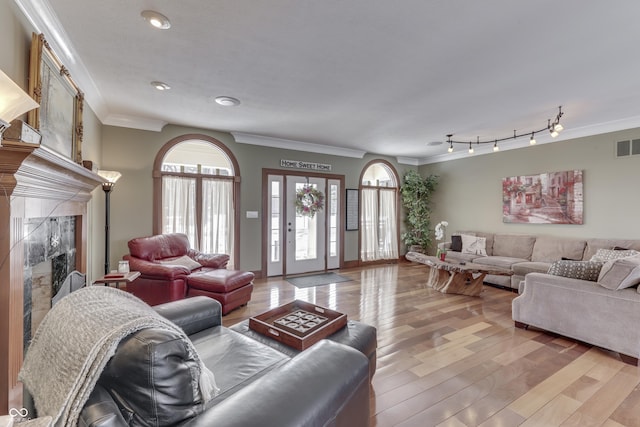 living room with visible vents, rail lighting, crown molding, light wood-style floors, and a fireplace