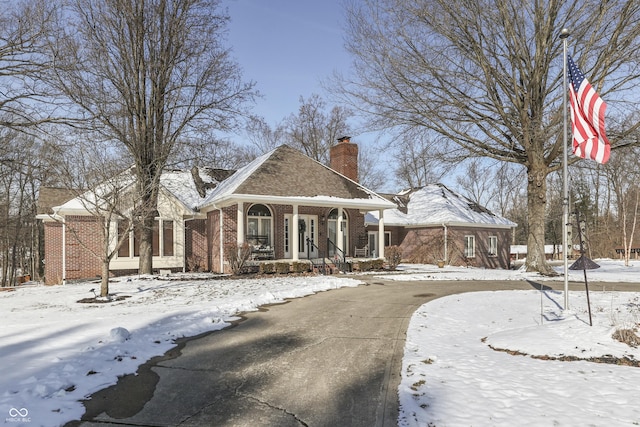 view of front of property with covered porch, brick siding, and a chimney