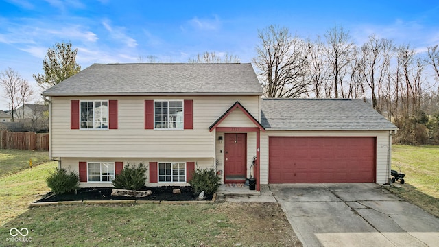 tri-level home with a garage, a shingled roof, fence, driveway, and a front lawn