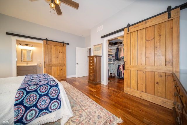 bedroom with a barn door, visible vents, a walk in closet, and wood finished floors