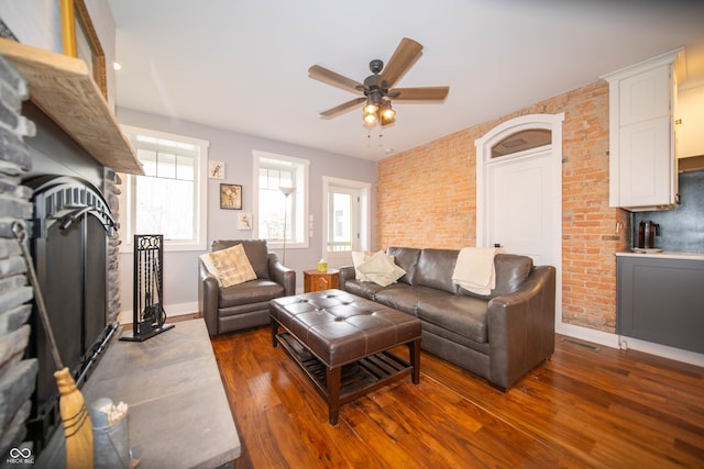 living room featuring dark wood-type flooring, baseboards, ceiling fan, and brick wall