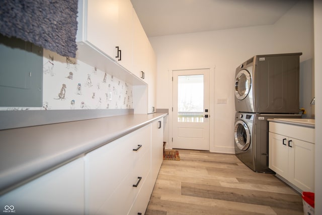 washroom featuring stacked washing maching and dryer, light wood-style flooring, and cabinet space