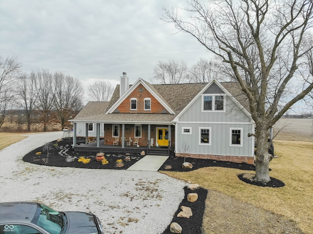 view of front facade with a shingled roof, a chimney, aphalt driveway, a porch, and board and batten siding