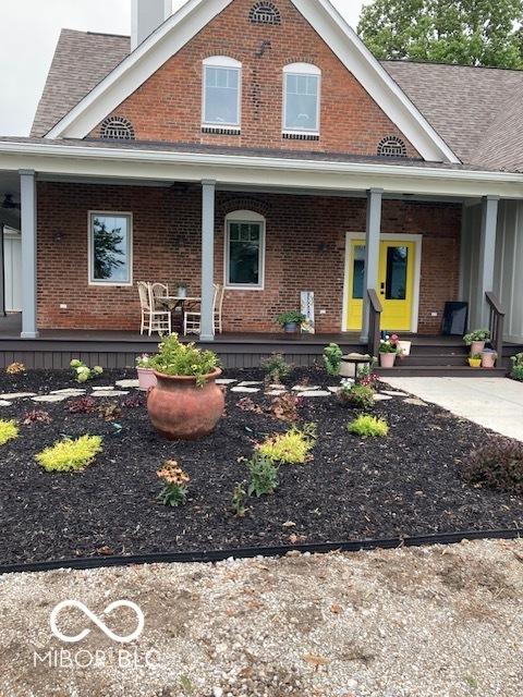 view of front of house with covered porch, brick siding, and roof with shingles