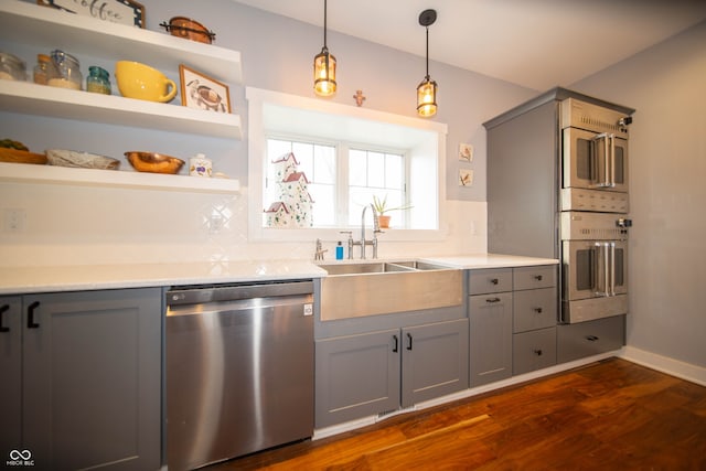 kitchen with a sink, appliances with stainless steel finishes, backsplash, gray cabinets, and dark wood finished floors