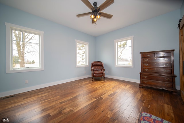 interior space featuring visible vents, a barn door, a ceiling fan, wood finished floors, and baseboards