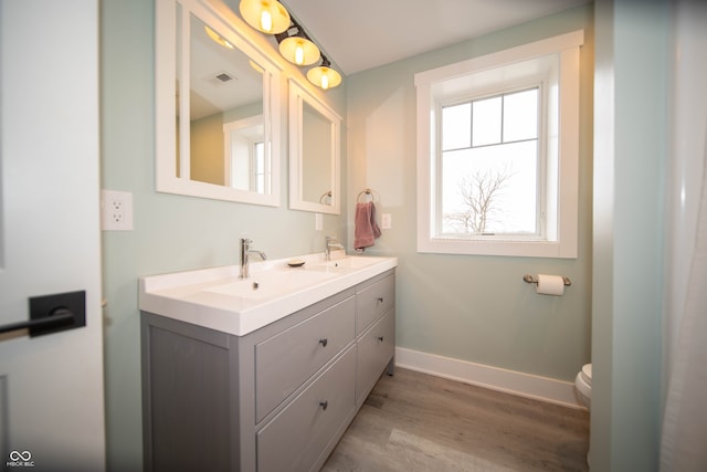 bathroom with double vanity, visible vents, a sink, wood finished floors, and baseboards