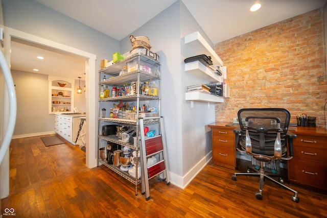 home office with brick wall, dark wood-style flooring, built in features, and baseboards